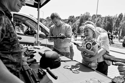 Un niño sostiene una pistola mientras su padre prueba un rifle durante un picnic militar en Polonia en 2022.