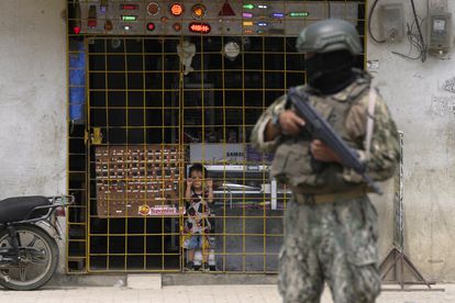 Un niño observa desde detrás del enrejado de una tienda mientras un soldado hace guardia en un puesto de seguridad, en Durán, el 14 de agosto de 2023.