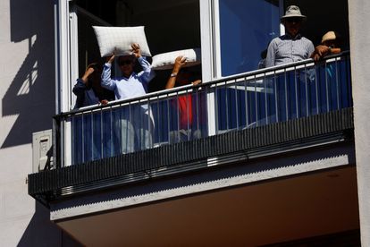 Varios vecinos se protegen del sol en una terraza mientras siguen el mitin del PP en Madrid.