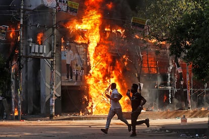 Dos hombres corren frente a un centro comercial incendiado durante las protestas de este domingo contra la primera ministra Sheikh Hasima.