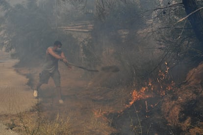 Un vecino lanza tierra con una pala sobre las llamas en Dioni, al noroeste de Atenas, este lunes.